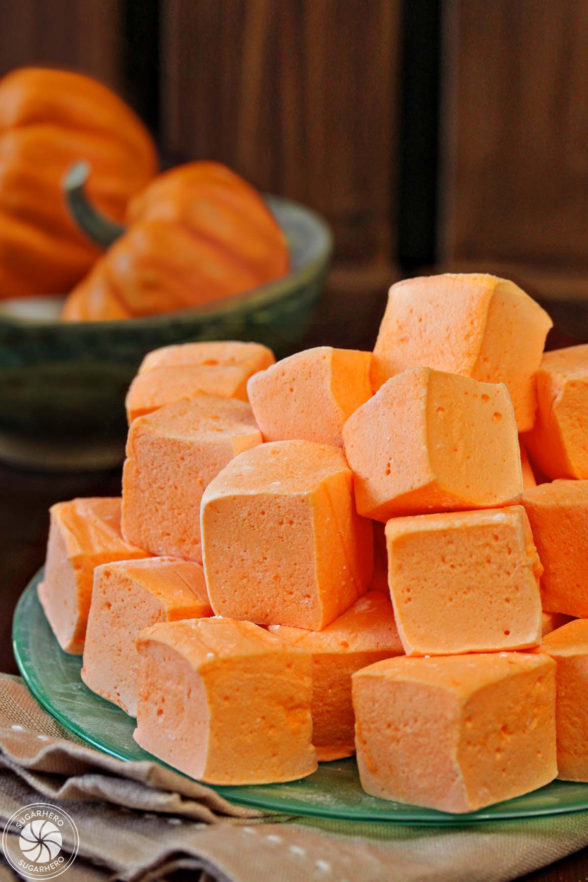 Pile of orange pumpkin marshmallows on a green plate, with small pumpkins in the background.