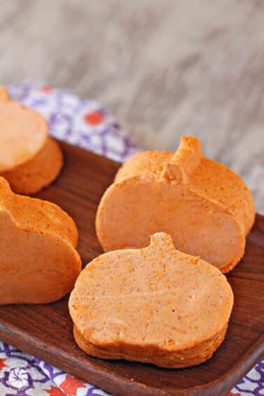 Pumpkin marshmallows, cut in the shape of pumpkins, on a wooden serving platter.