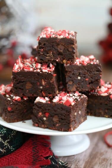 A pyramid of cut Peppermint Crunch Brownies on a white cake plate.