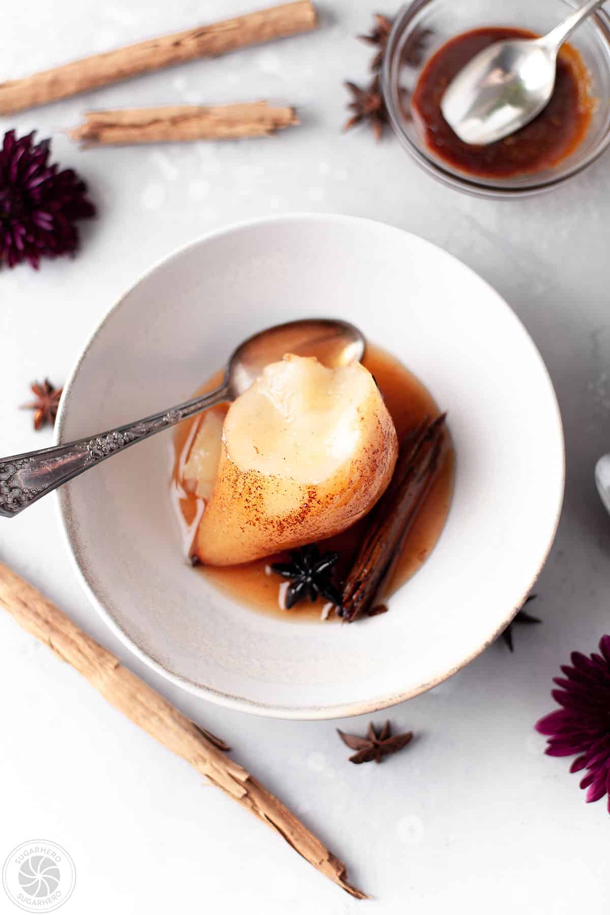 A Poached Pear with a bite removed next to a silver spoon.