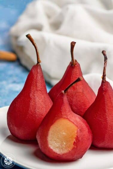 4 Red Wine Poached Pears on a small white plate with a bite removed from the front pear.