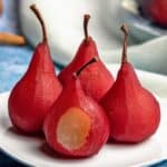 4 Red Wine Poached Pears on small white plate with a bite removed from the front picture.