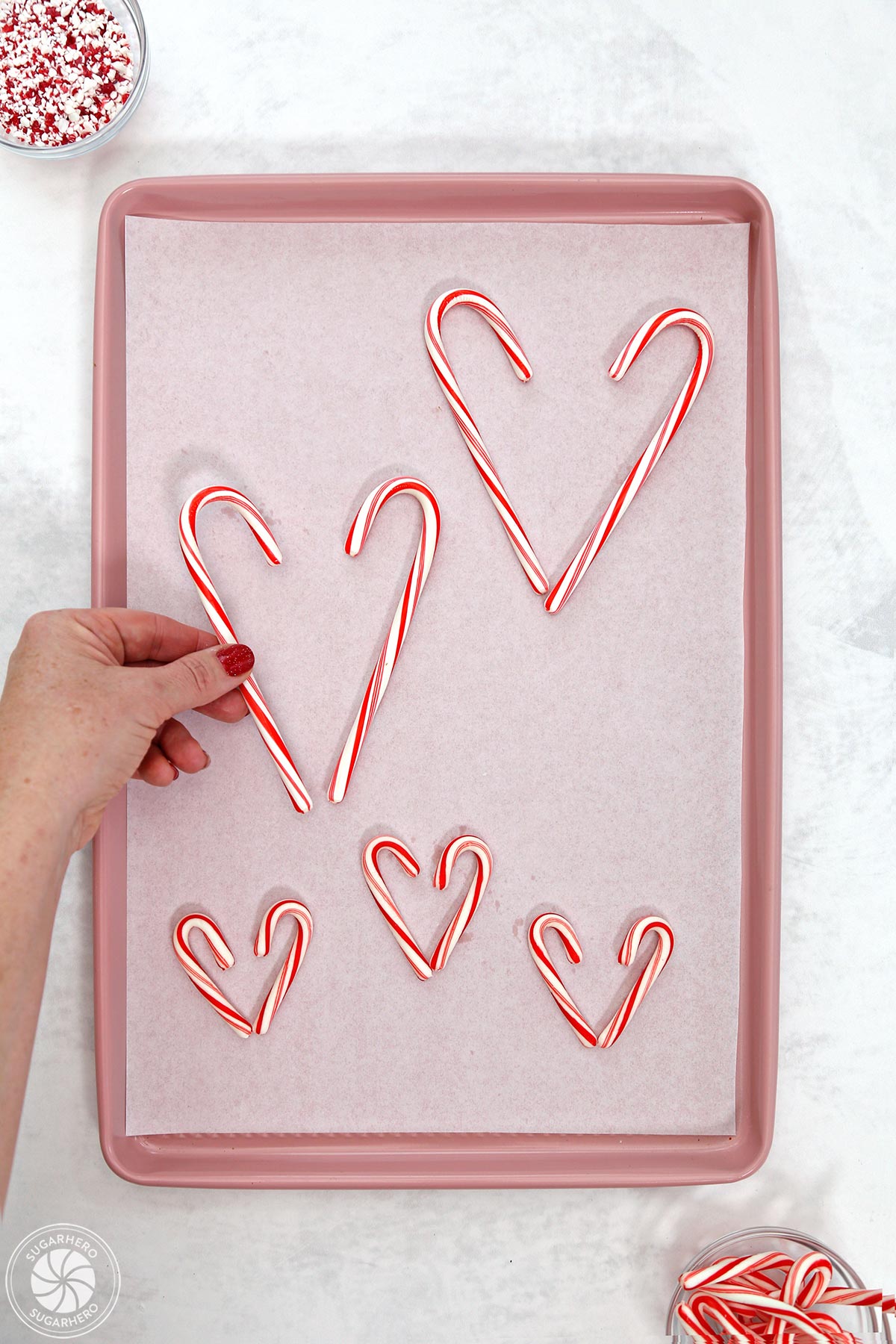 Placing candy canes on a parchment-covered pink baking sheet.