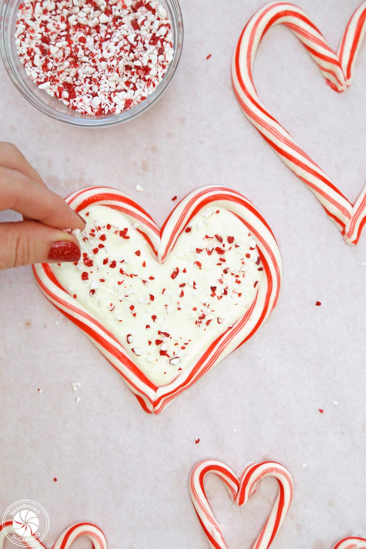Hand sprinkling crushed candy cane pieces on white chocolate inside a candy cane heart.