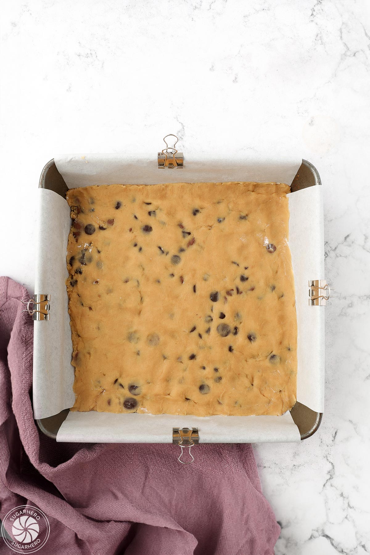 Chocolate chip cookie dough spread out in a layer on the bottom of a square baking pan.
