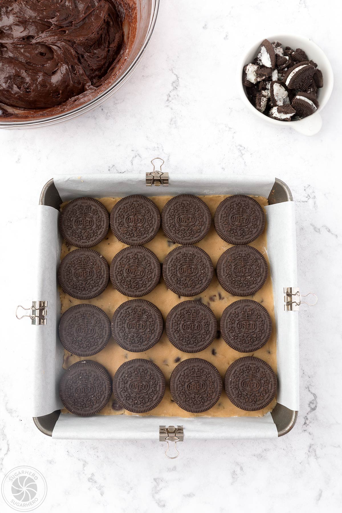 Rows of Oreos layered on top of chocolate chip cookie dough in a square pan.