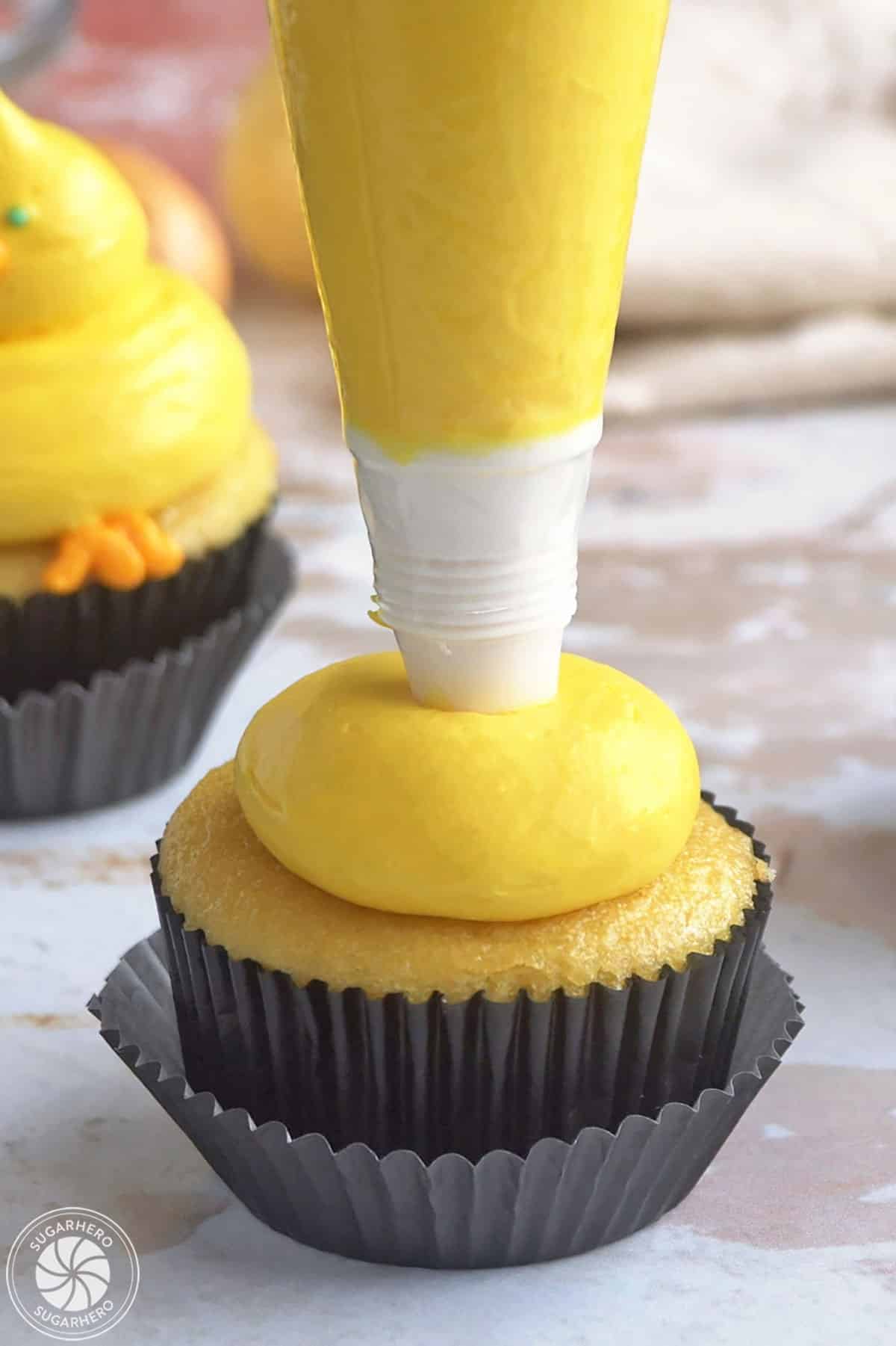 Adding a large buttercream dollop on top of a cupcake to make baby chick cupcakes.