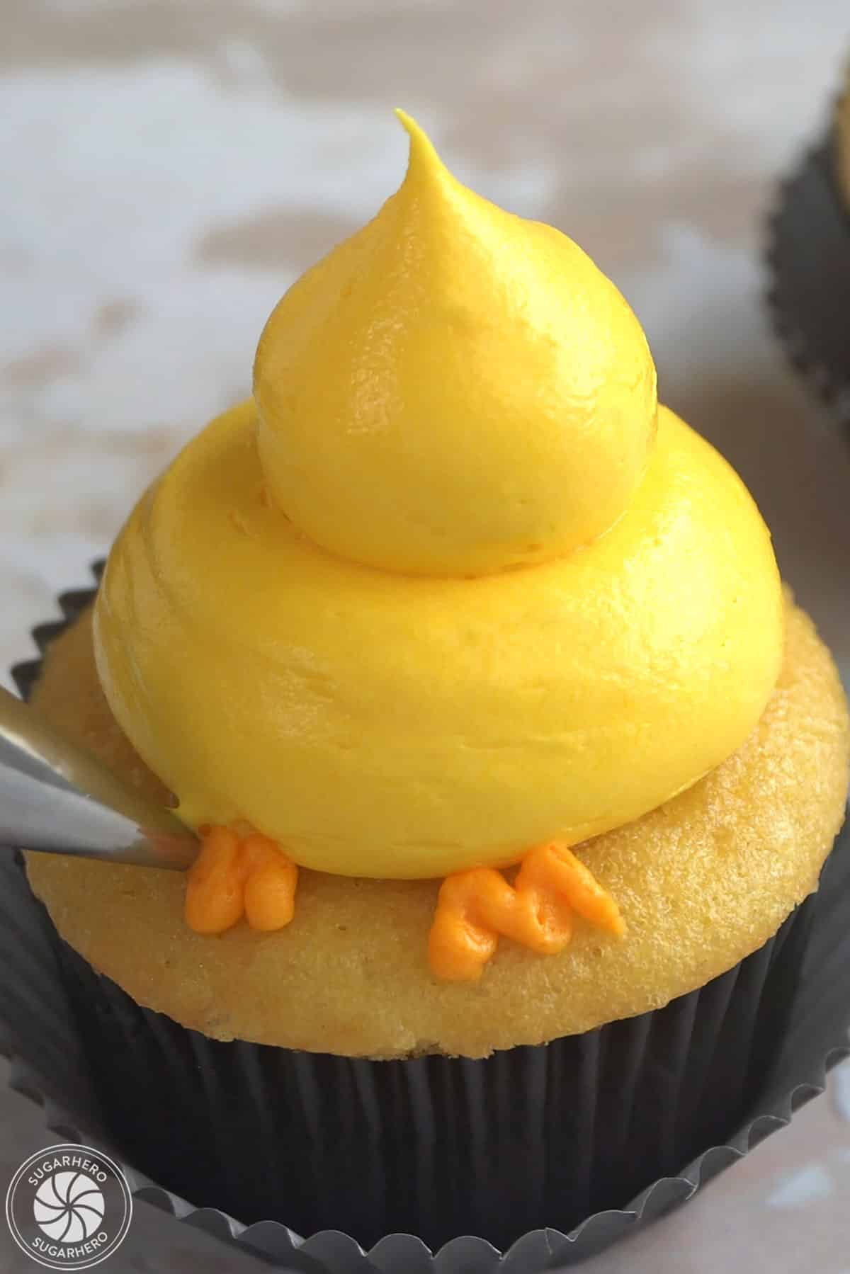 Piping orange buttercream feet onto a baby chick cupcake.