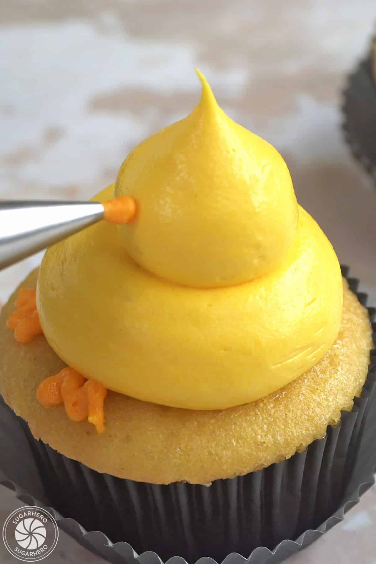 Piping an orange buttercream beak on a baby chick cupcake.