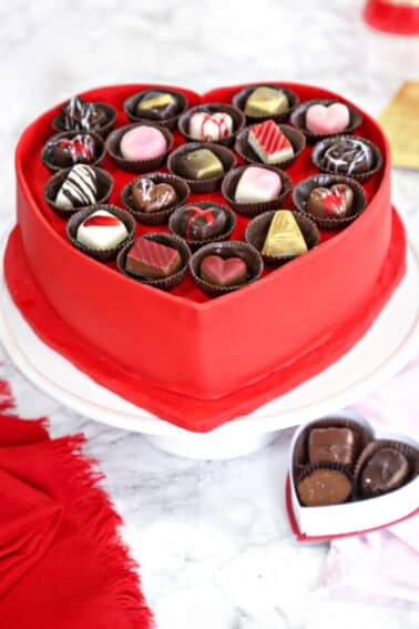 Heart-shaped Box of Chocolates Cake on a white cake stand with a mini box of chocolates below.