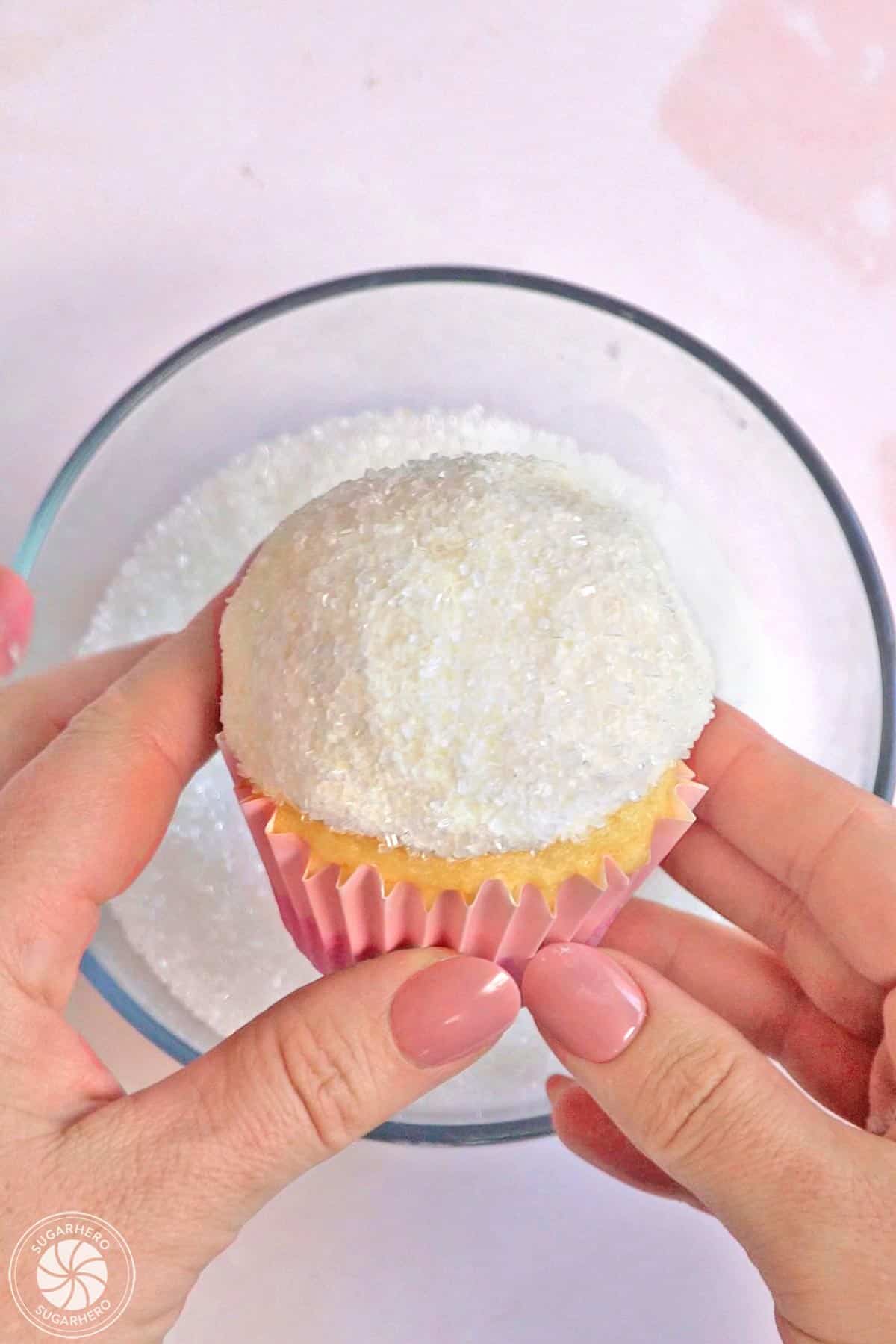 Rolling the top of a buttercream-covered cupcake in white sparkling sugar.