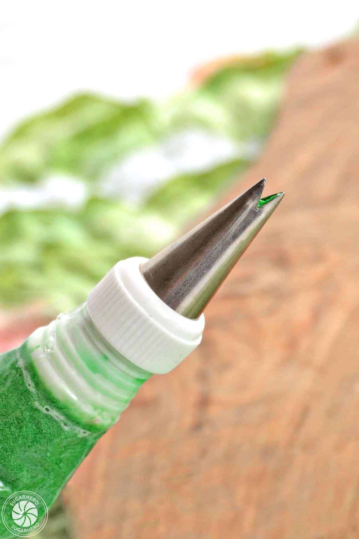 Close-up of a piping bag filled with green buttercream and fitted with a leaf piping tip.