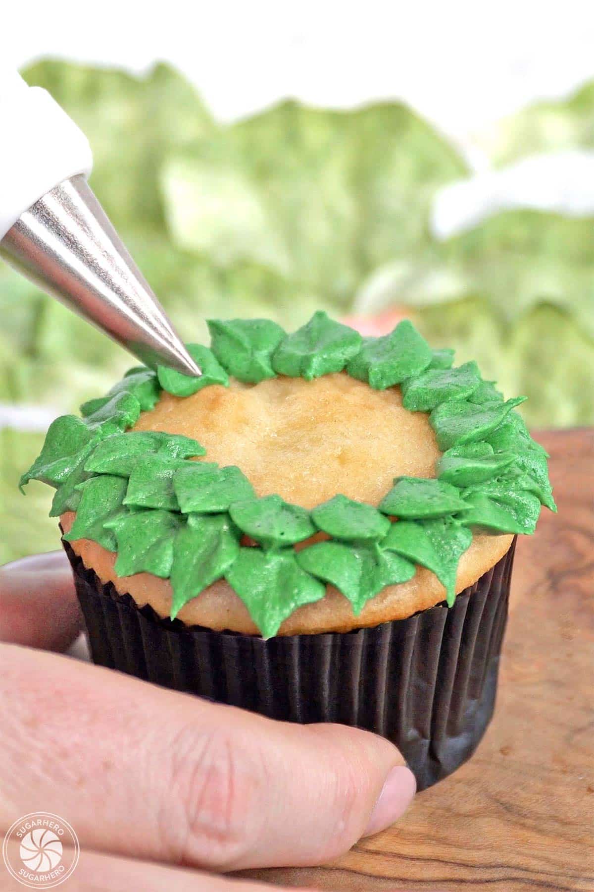 Piping green buttercream leaves on top of a vanilla cupcake.