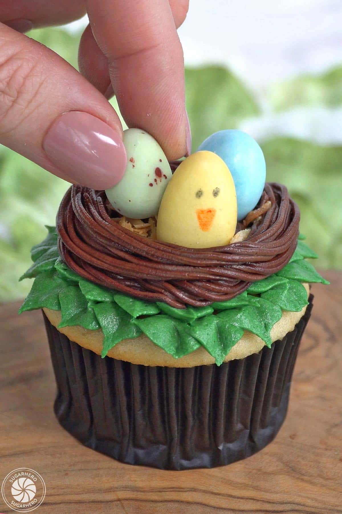 Placing candy eggs into a buttercream nest on top of a cupcake.