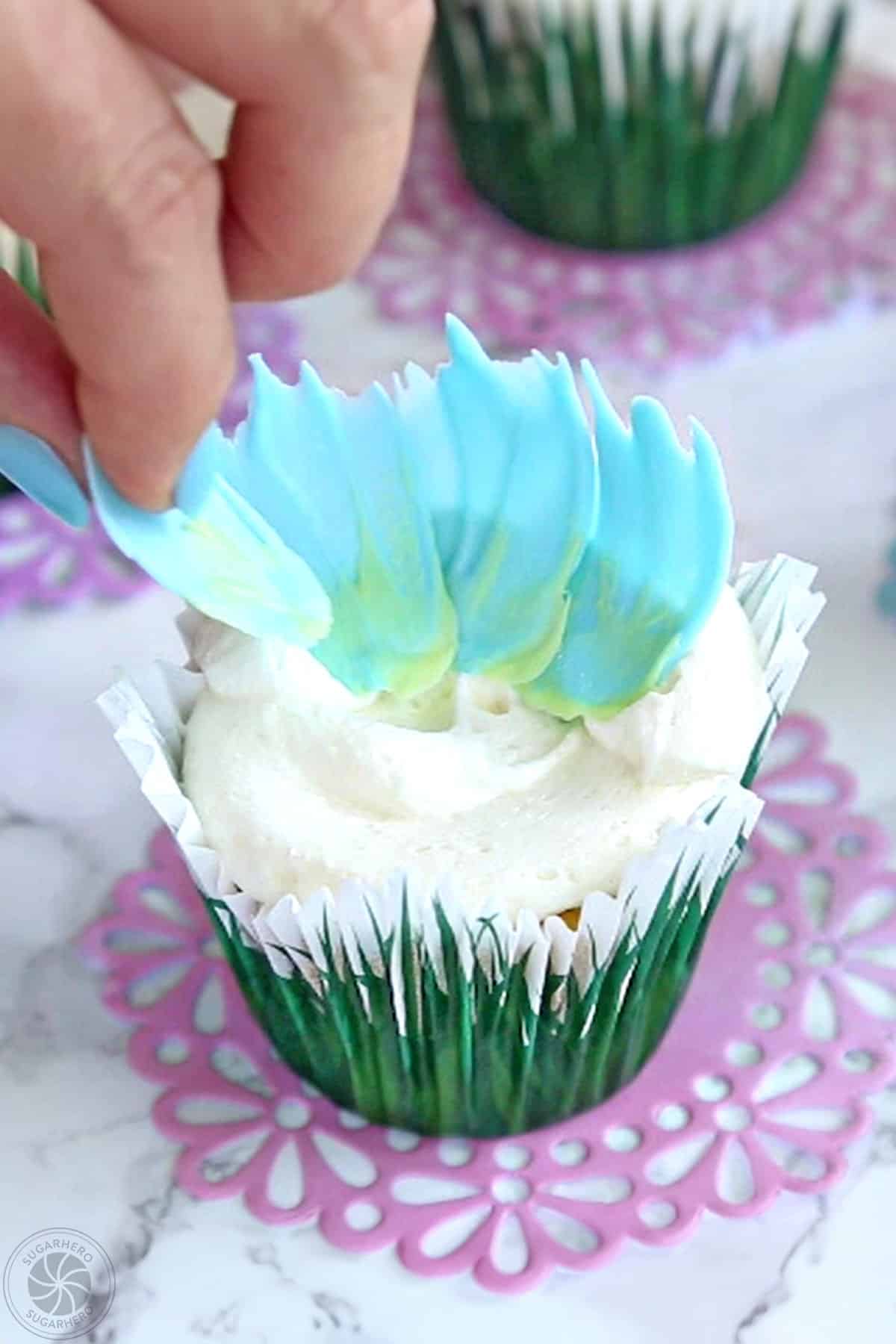 Placing blue candy melt petals on top of a buttercream-covered cupcake.