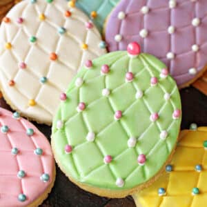 A pile of Fondant-Covered Easter Egg Cookies on a wooden surface.