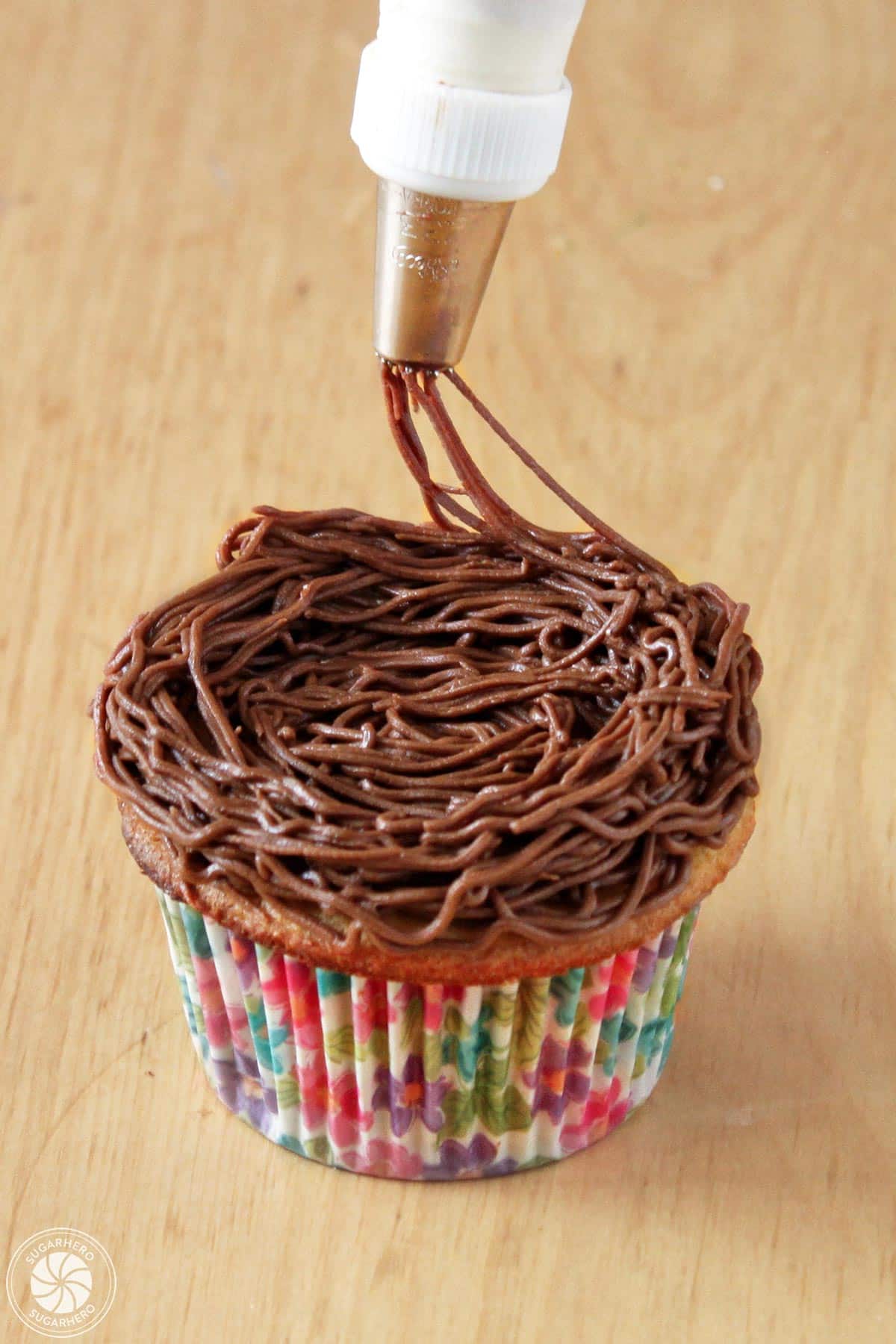 Piping a chocolate buttercream nest around the outside edge of a cupcake.