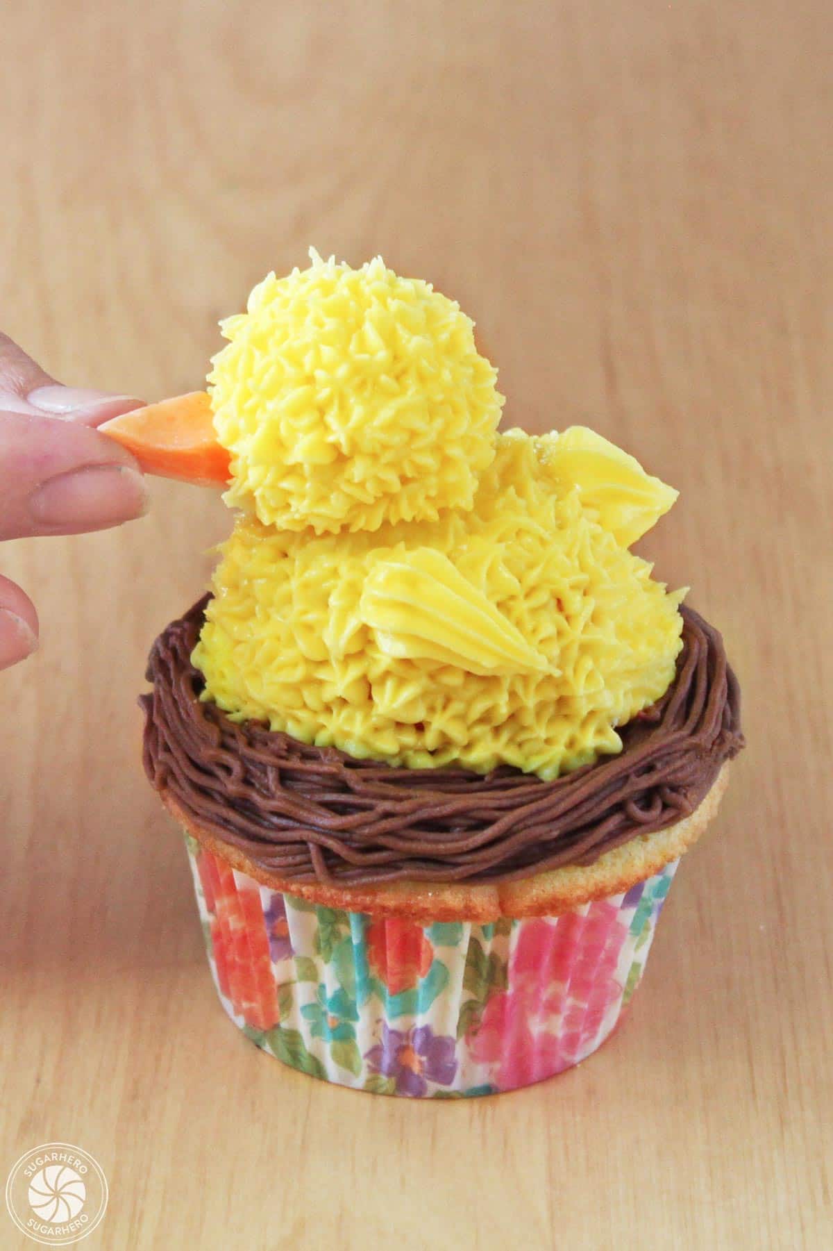 Adding an orange candy beak to an edible Easter chick on top of a cupcake.