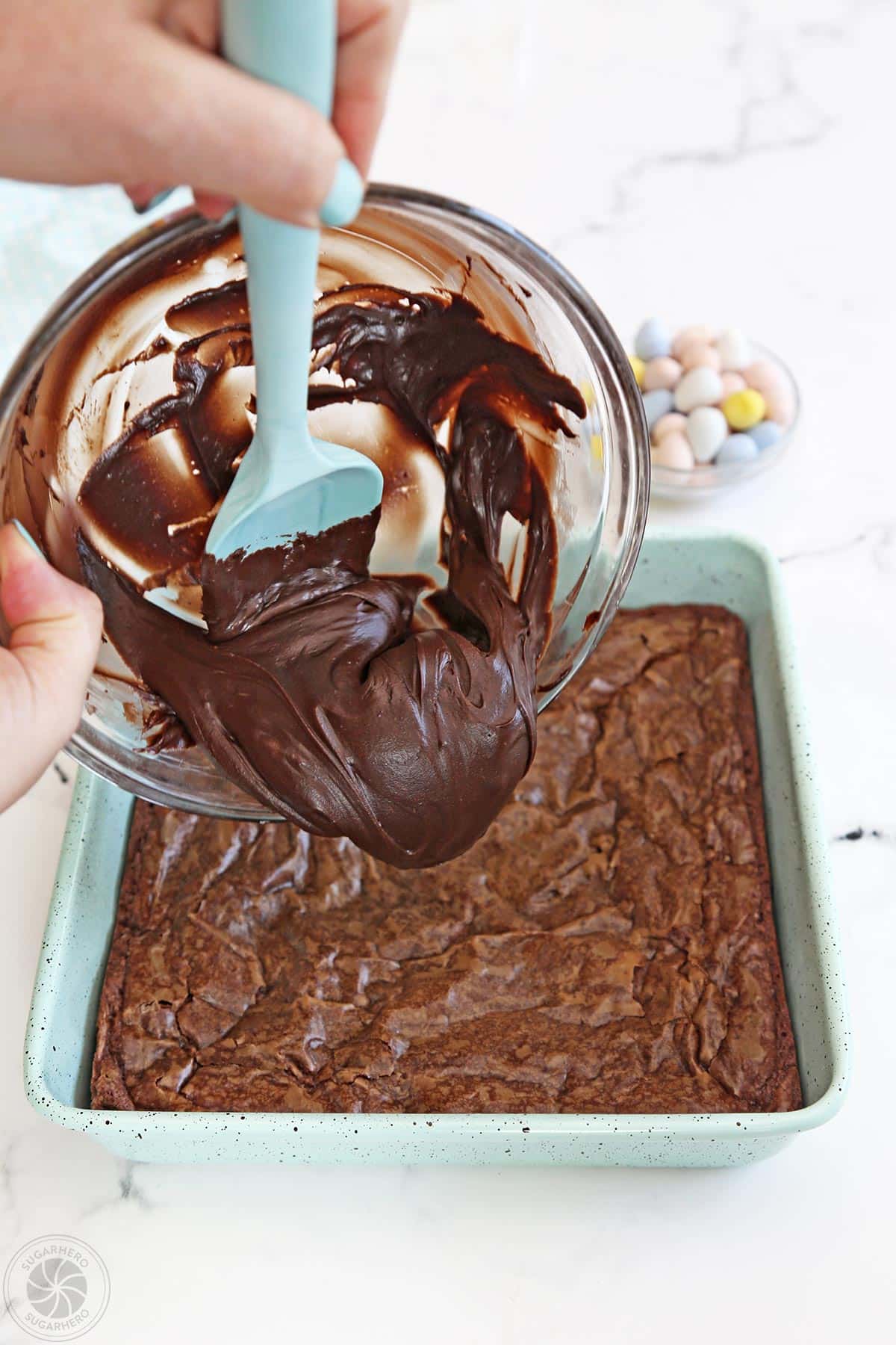 Scraping chocolate frosting on top of a pan of brownies.