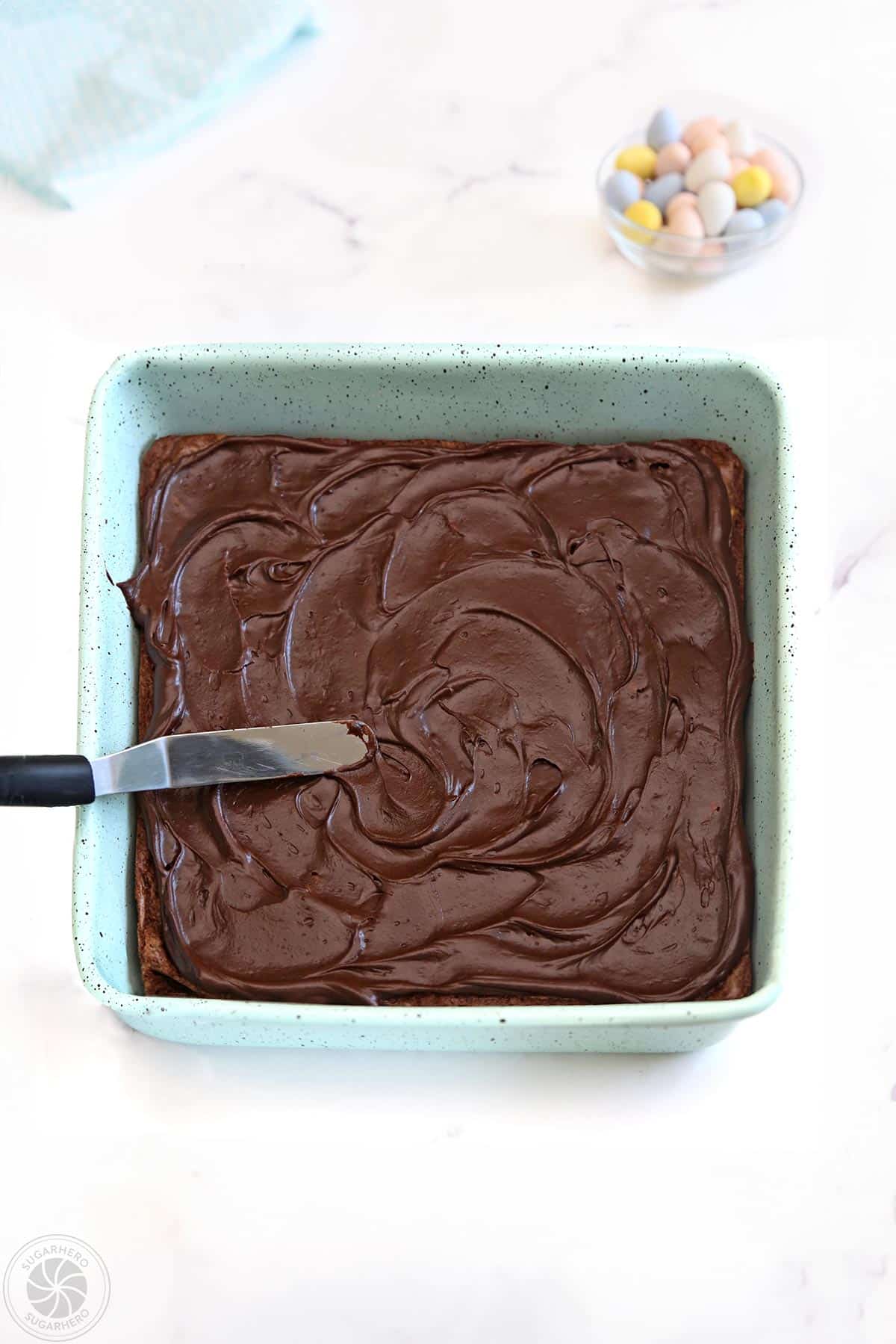Spreading glossy chocolate frosting on top of a pan of brownies.