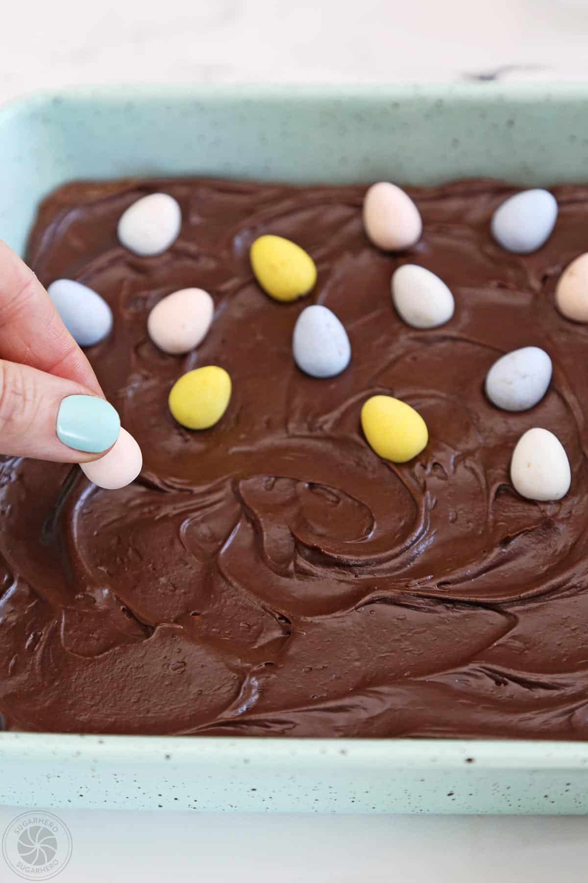 Placing colorful Cadbury mini eggs on top of frosted brownies.