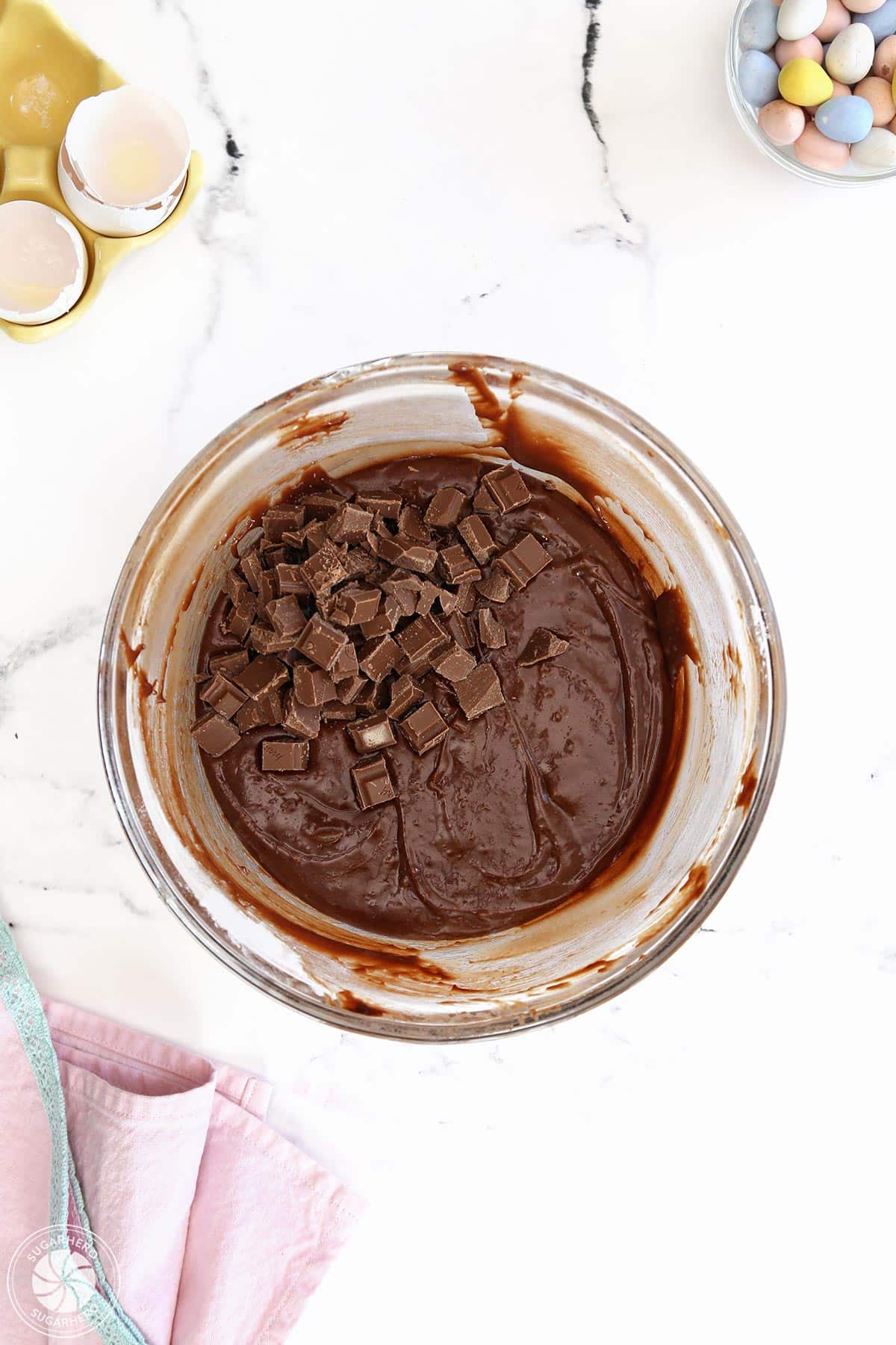 Stirring chopped chocolate into brownie batter in a glass bowl.