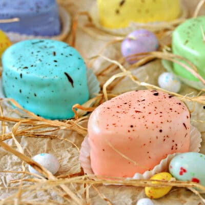 Selection of pastel Easter Egg Petit Fours next to raffia and Easter candy.