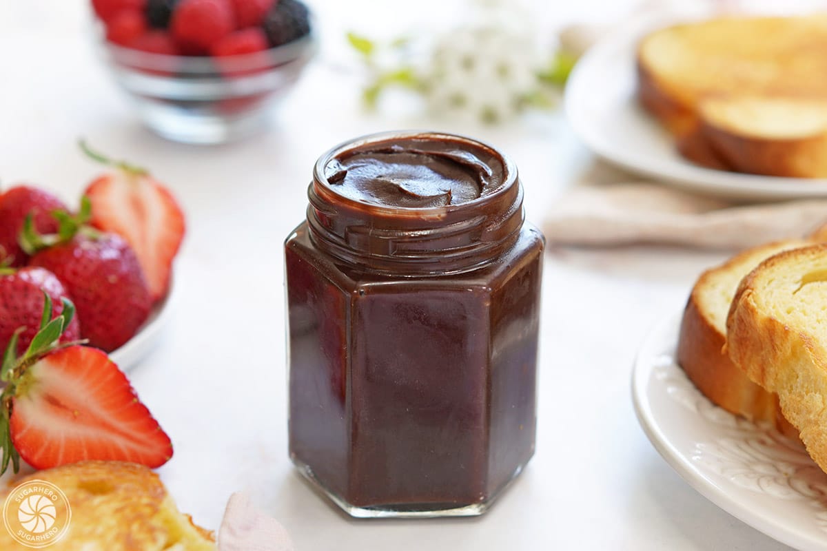 A glass jar of Chocolate Spread next to strawberries and bread.
