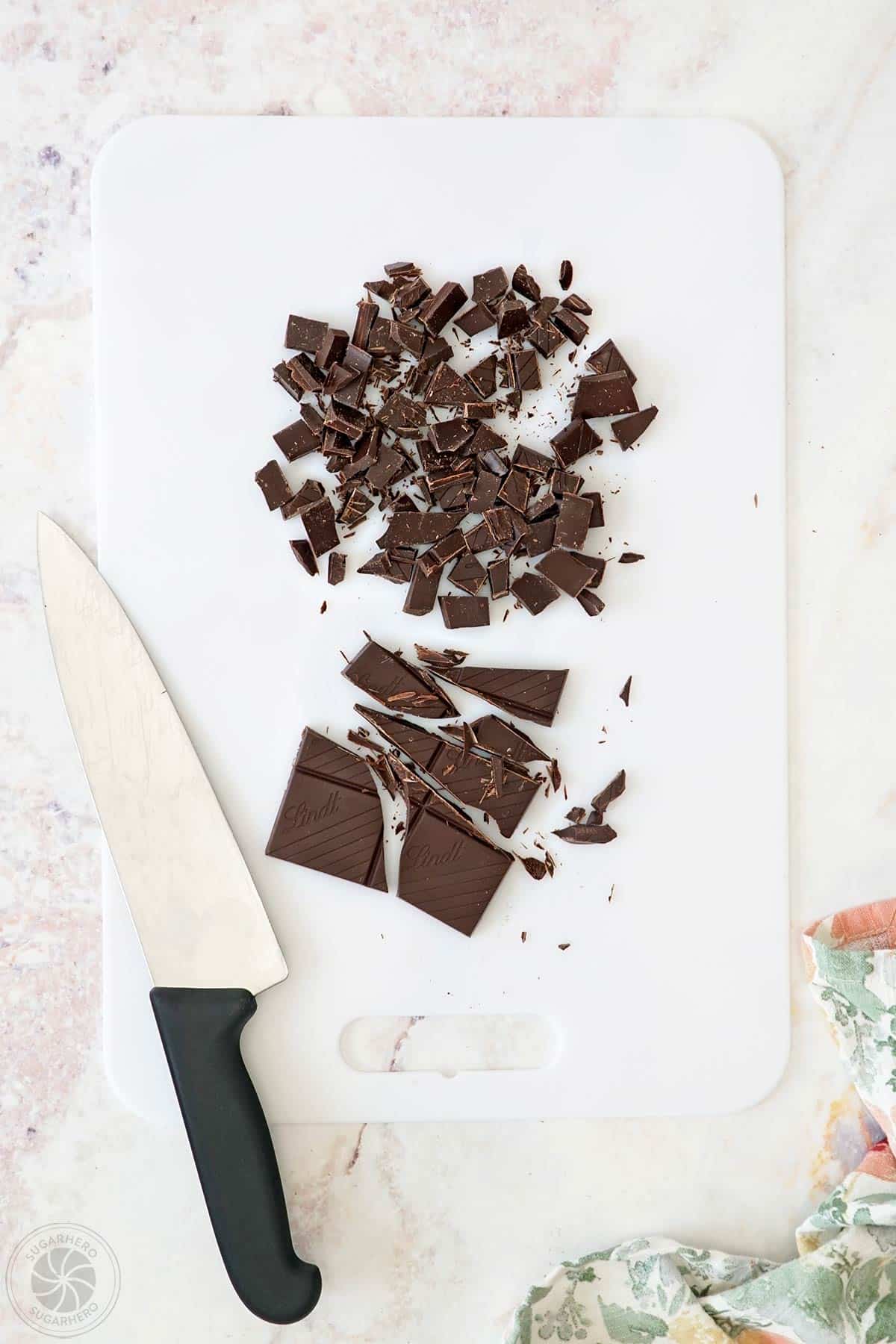 Chopped chocolate on a cutting board next to a knife.