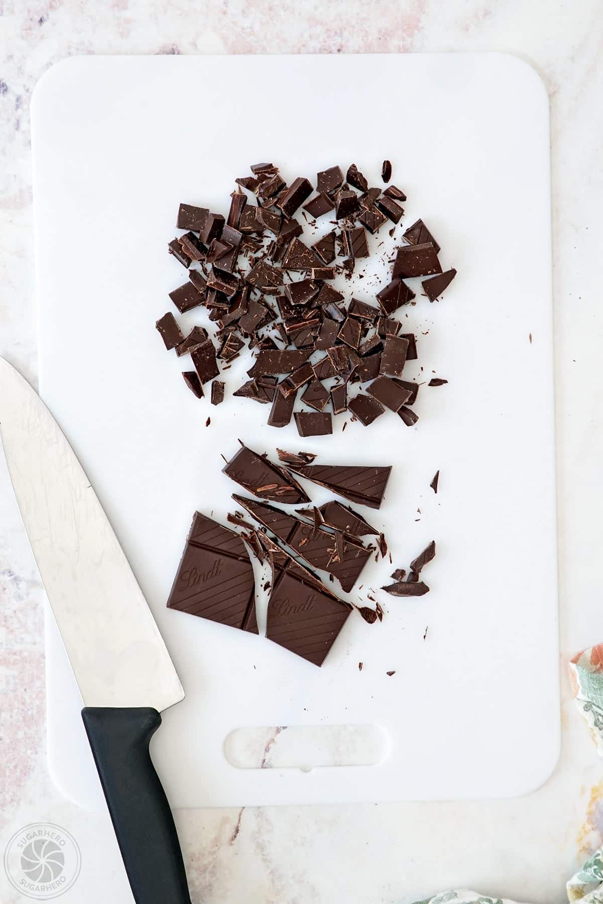 Chopped chocolate on a cutting board next to a knife.