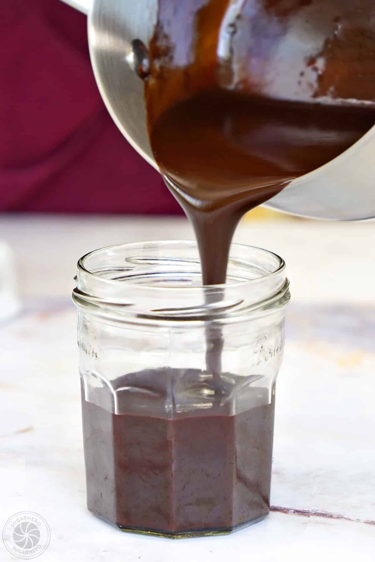 Hand pouring chocolate spread into a small glass jar.