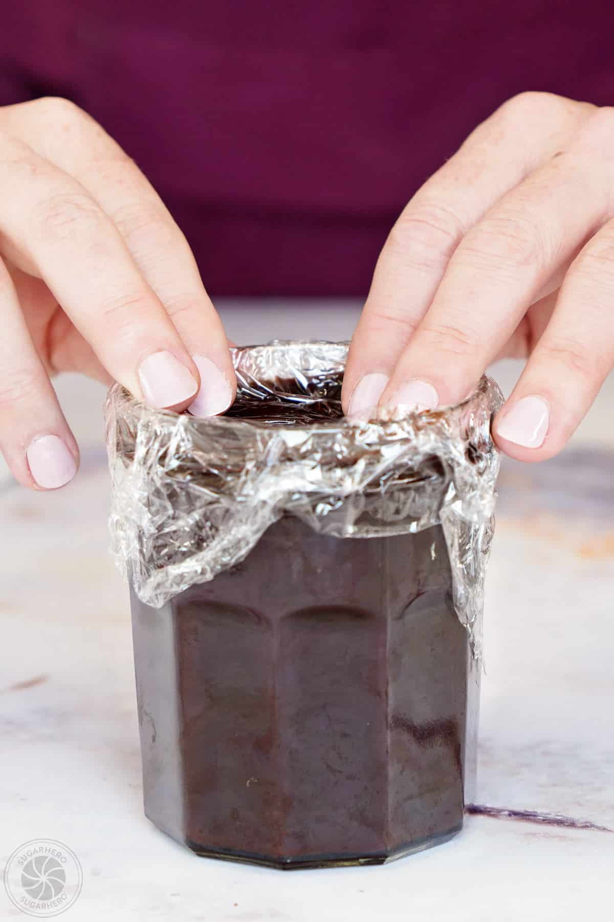 Hands pressing plastic wrap on the top of a jar of chocolate spread.