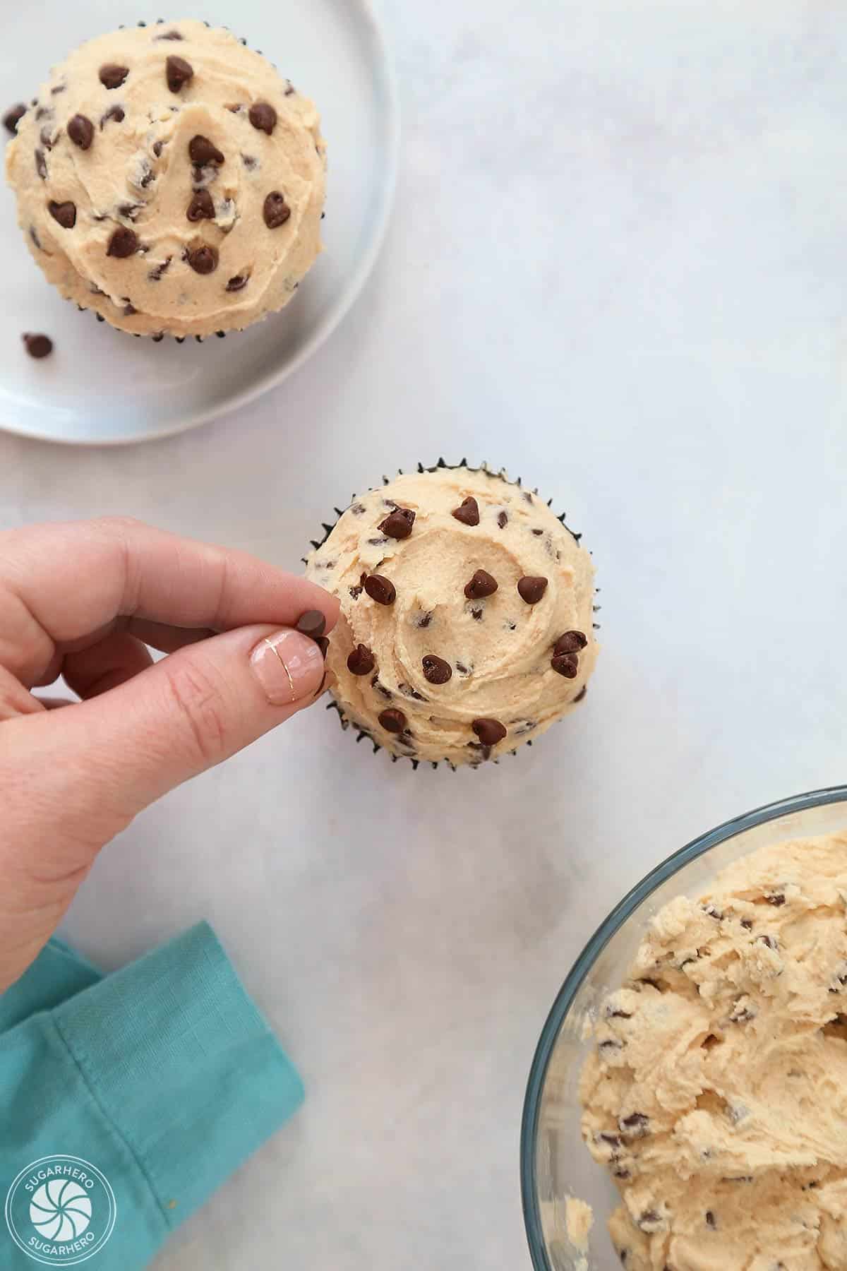 Hand placing mini chocolate chips to the top of frosting.