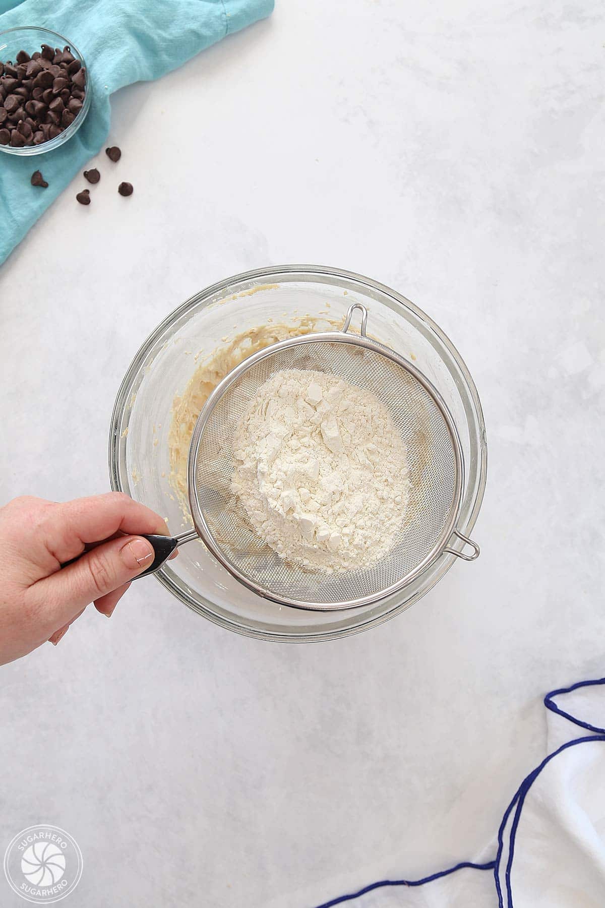 Hand sifting flour into the frosting mixture with a sieve.