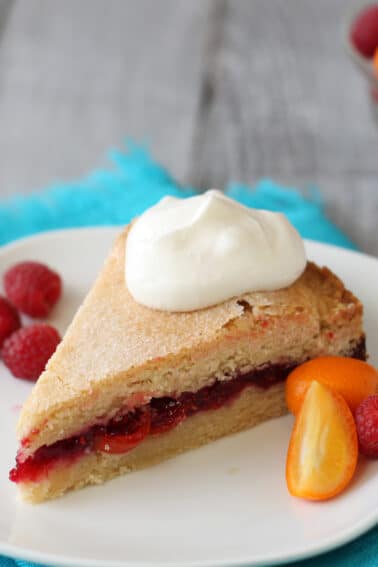 A slice of Raspberry Kumquat Sugar Cookie Cake on a white plate next to raspberries and kumquats.