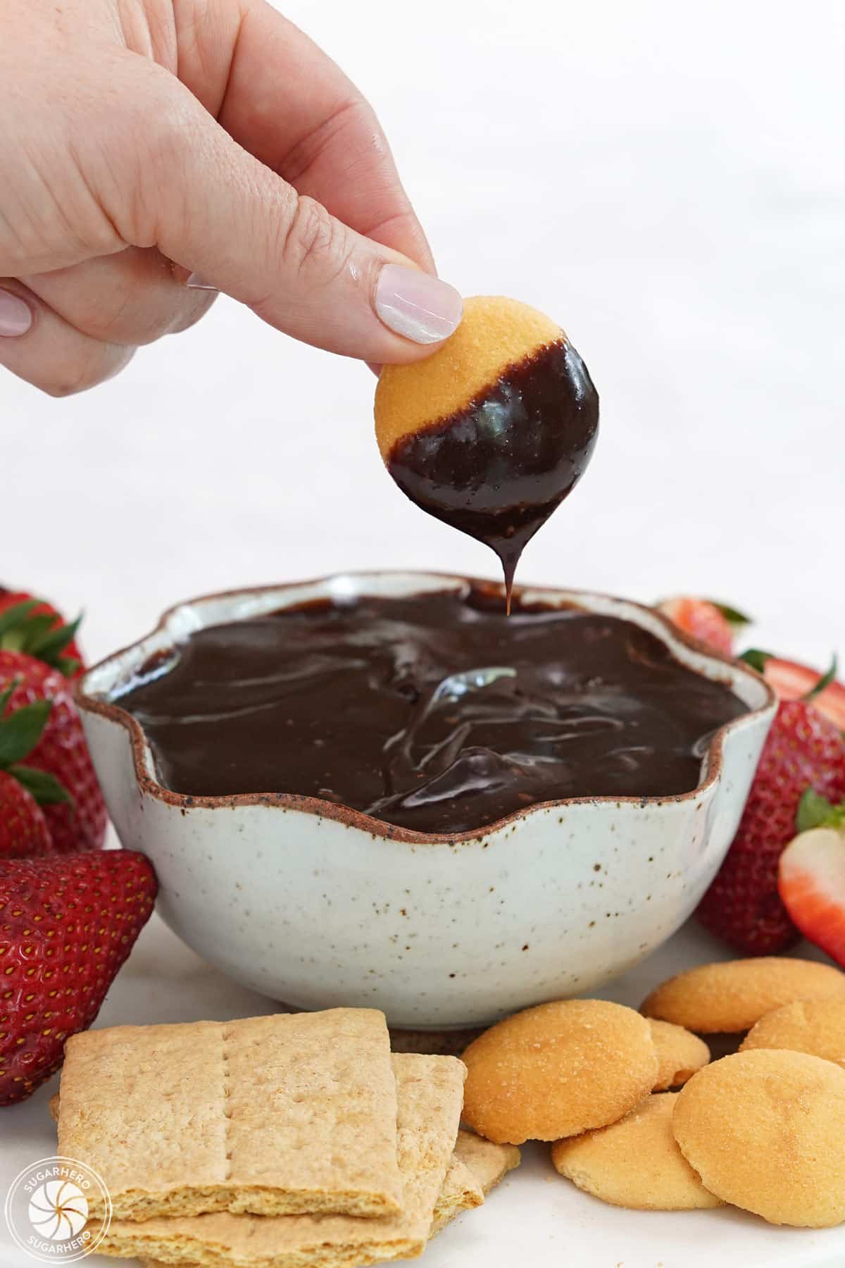 Hand holding a vanilla wafer half-dipped in chocolate spread.