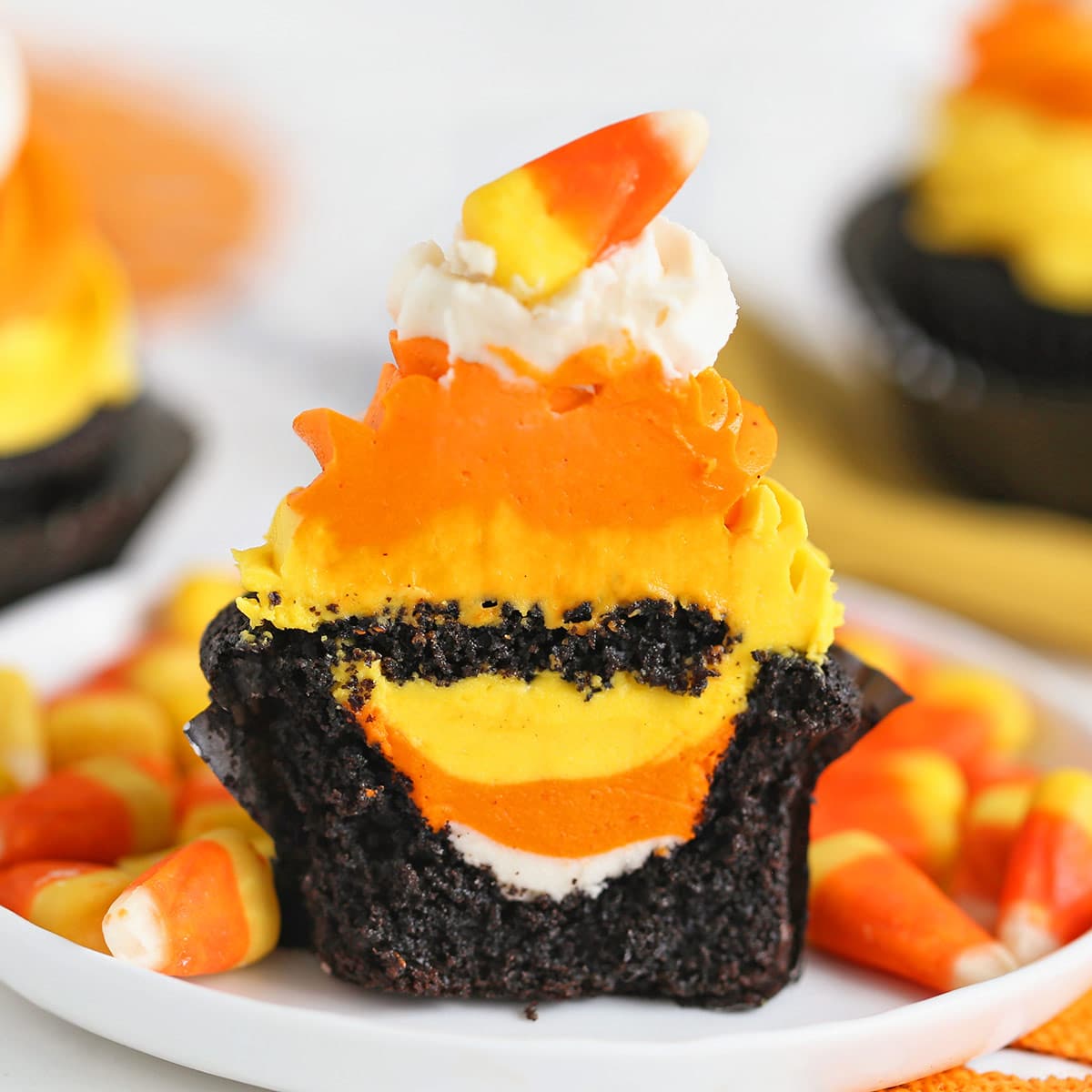 A Candy Corn Cupcake on a white plate, cut in half to show the hidden frosting candy corn inside.