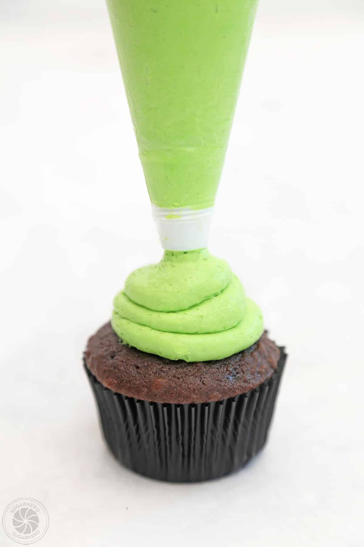 Piping a blob of green frosting on top of a cupcake.