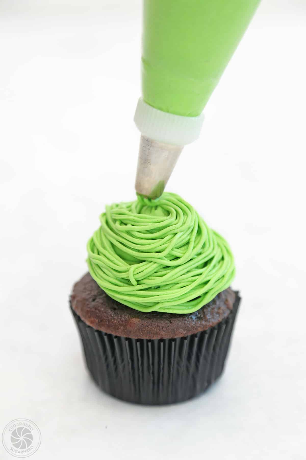 Using a grass piping tip to swirl green frosting strings on top of a Monster Cupcake.