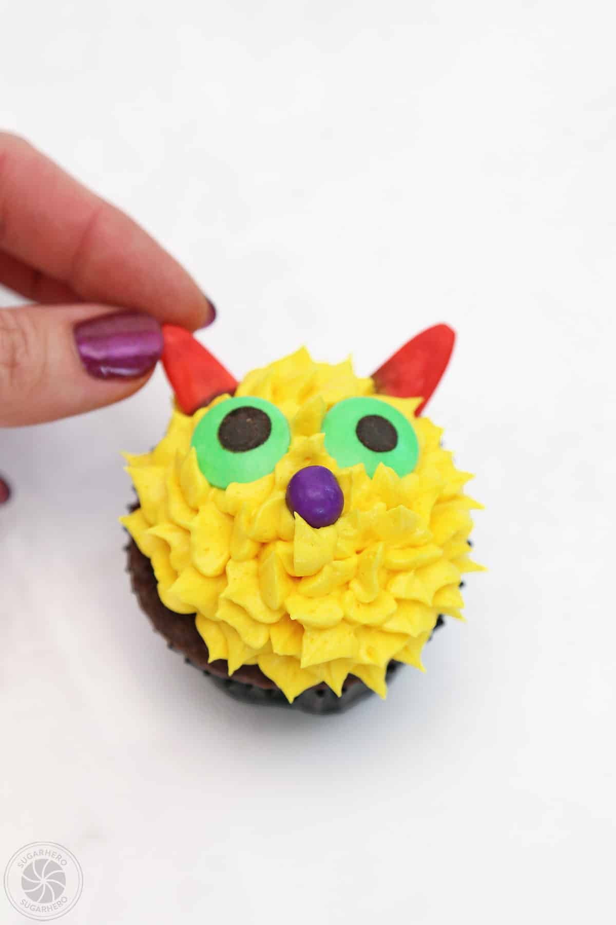 Hand placing candy horns on a yellow Monster Cupcake.