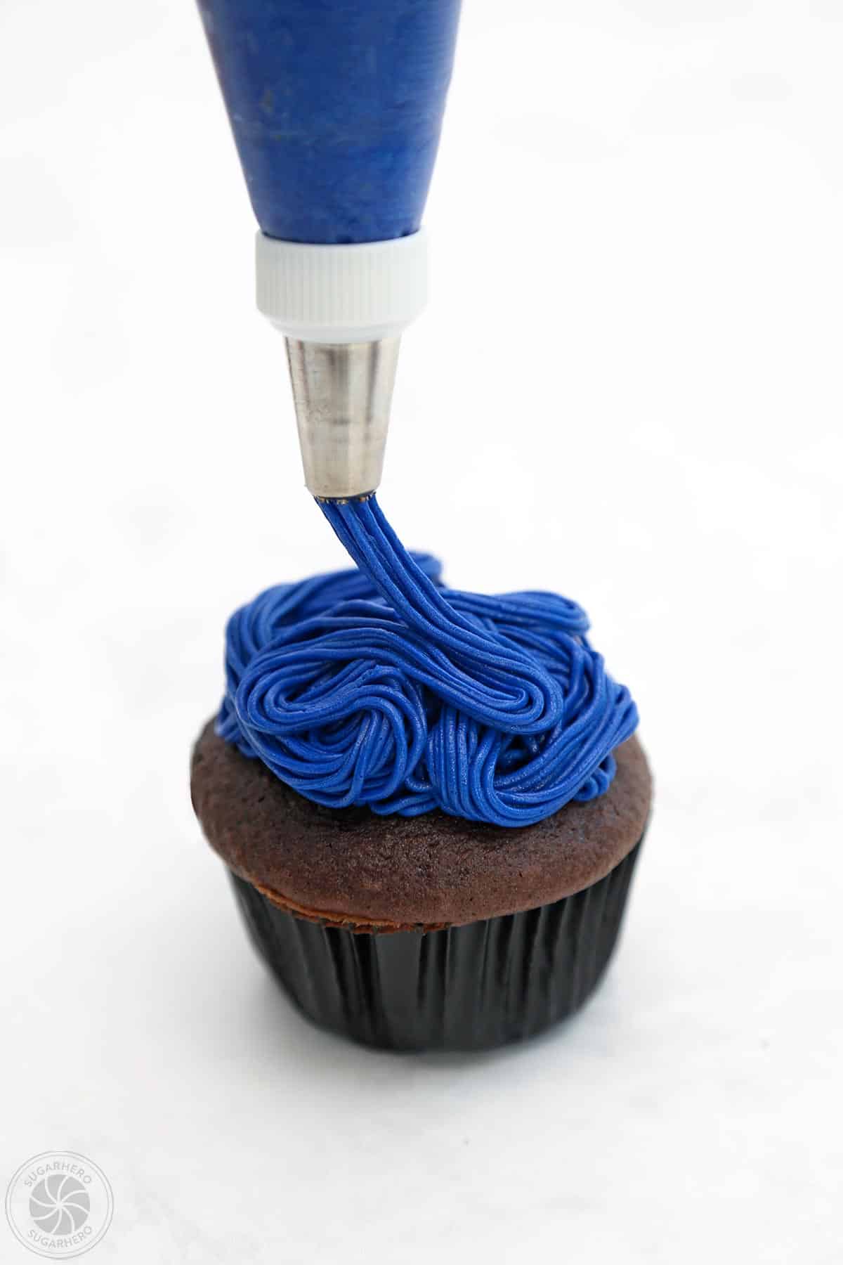 Using a grass tip to pipe strings of blue frosting on a cupcake.