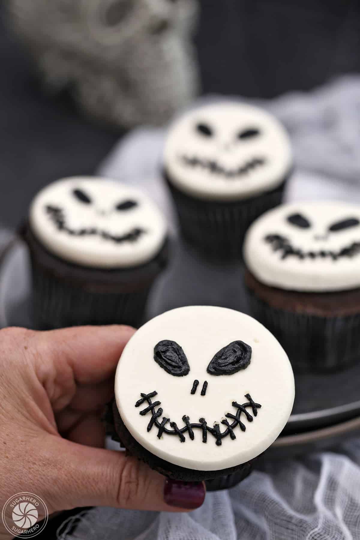 Hand holding a Skull Cupcake with more cupcakes in the background.