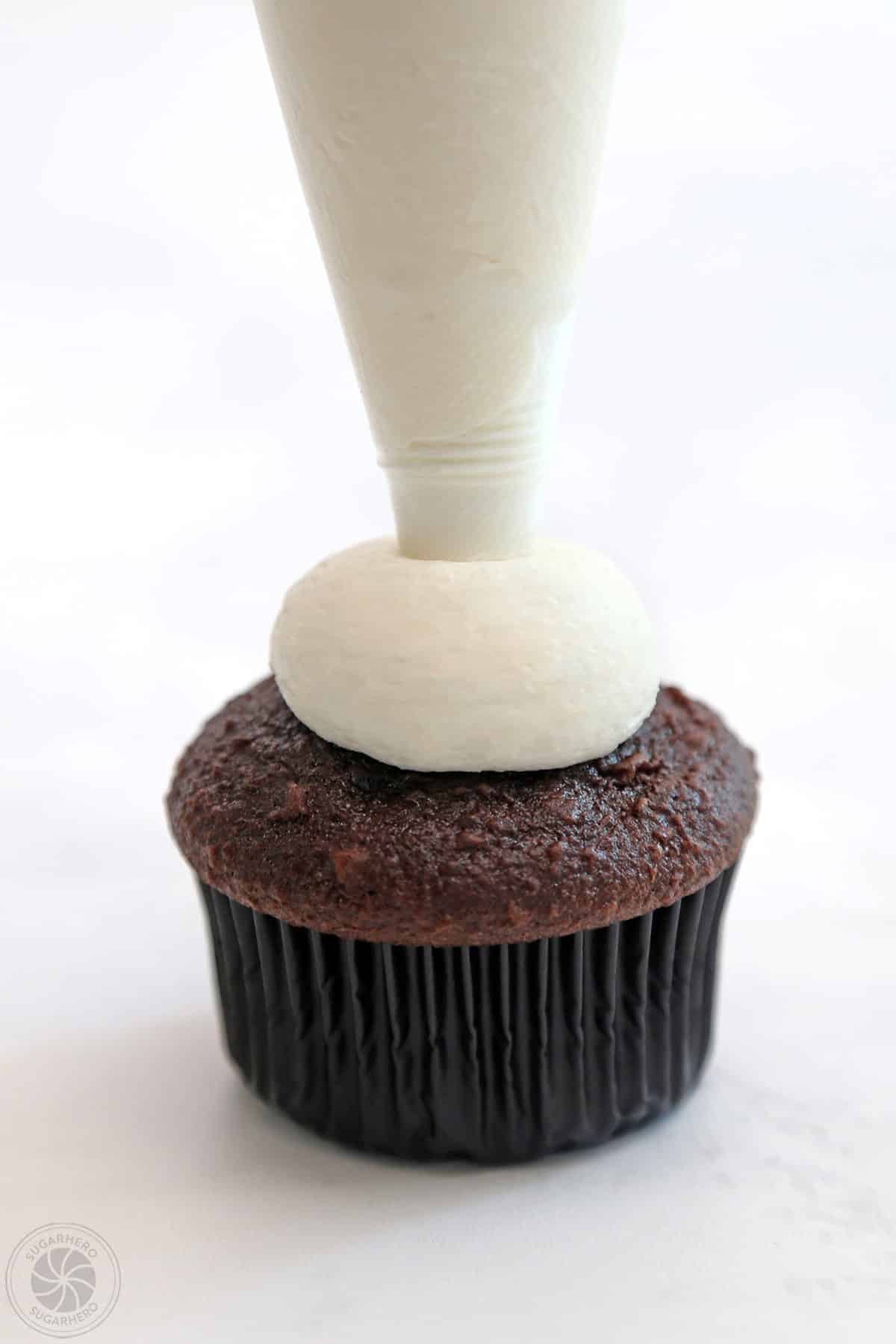 Piping a ball of white frosting on a chocolate cupcake.