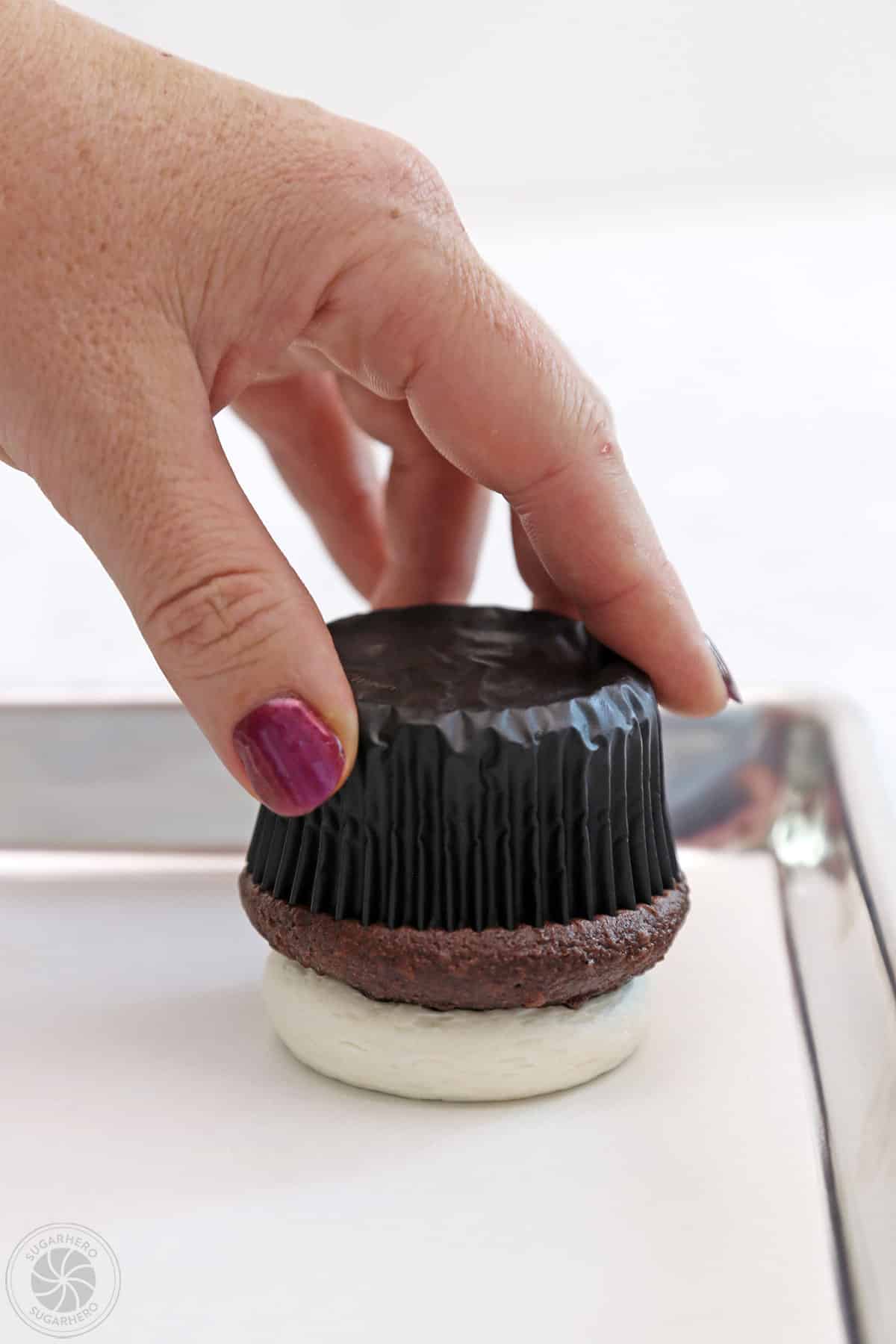 Turning a frosted cupcake upside down on a parchment lined baking sheet.
