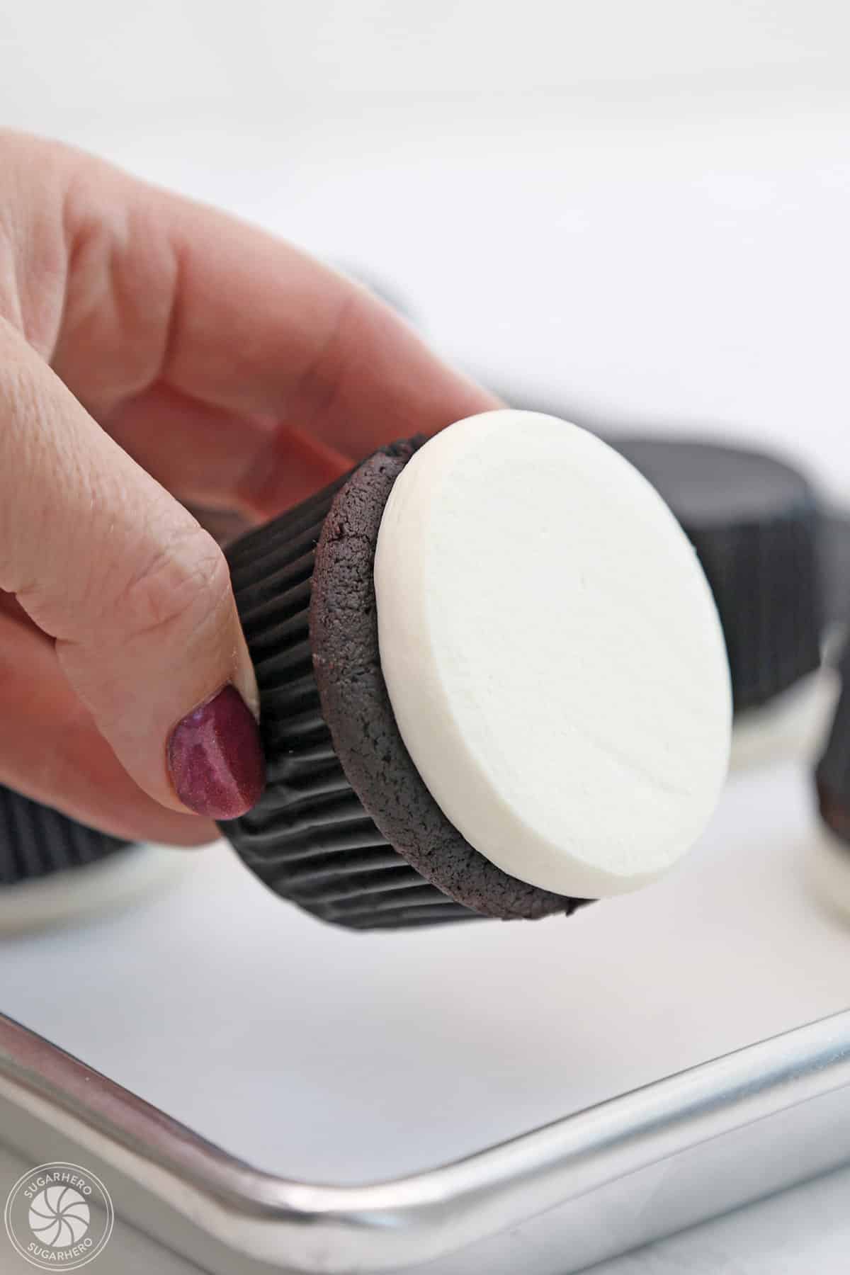 Hand showing a chocolate cupcake with flattened white buttercream.