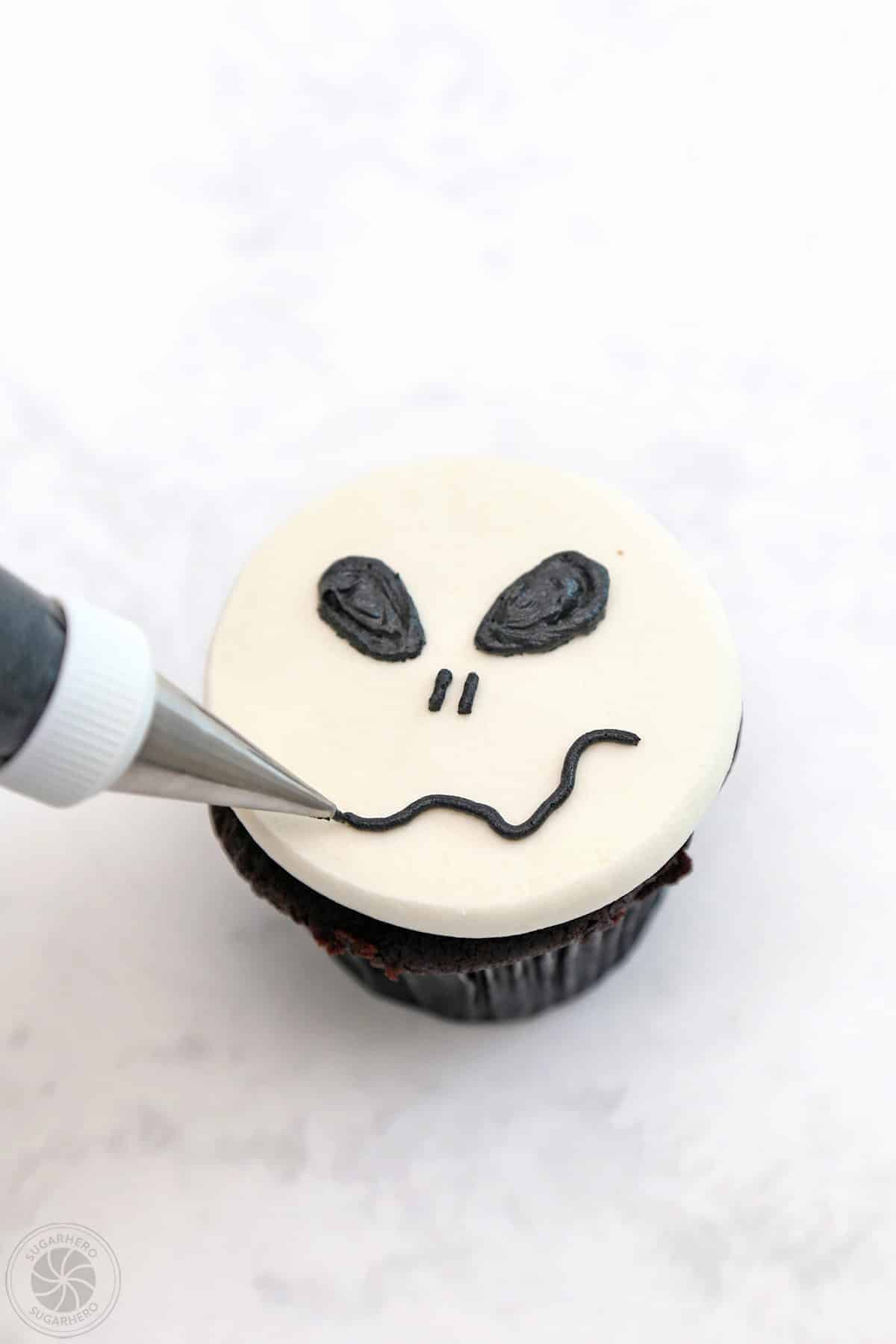 Piping a mouth onto a Skull Cupcake.