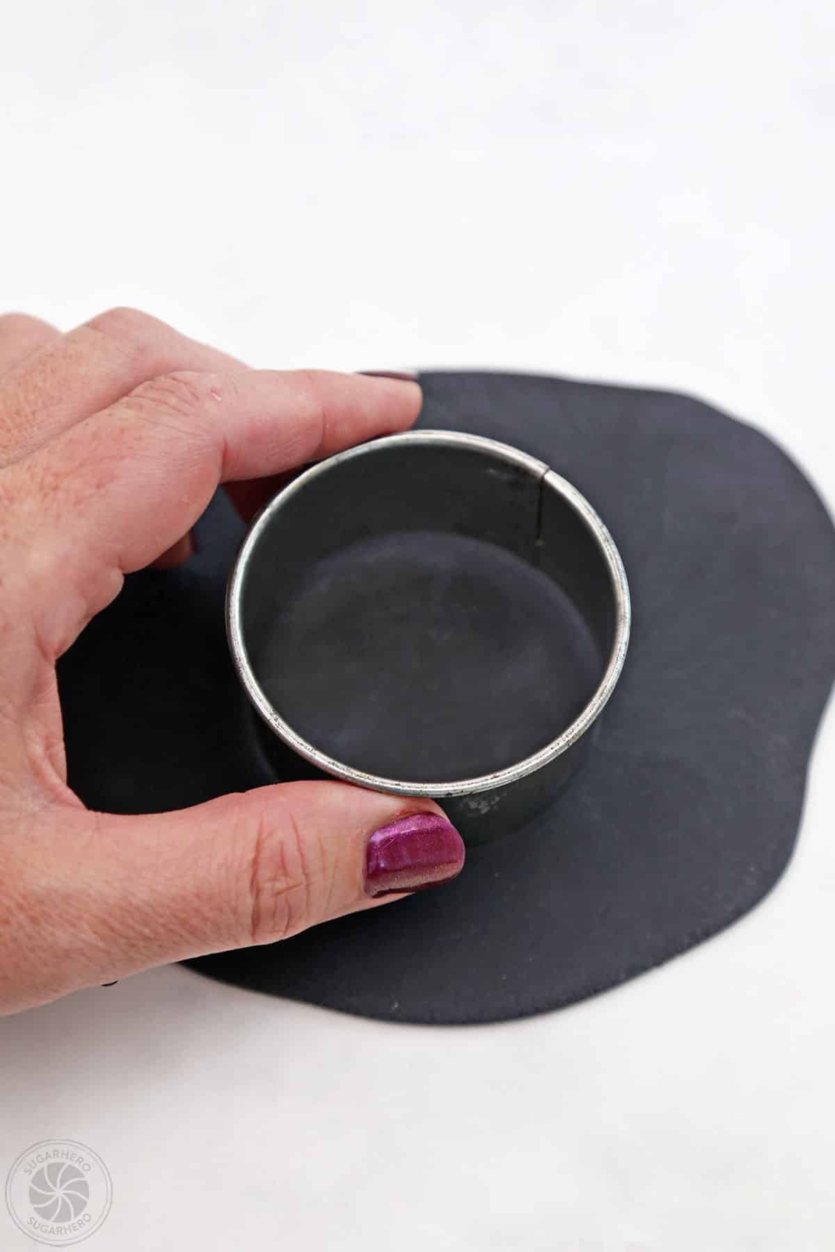 Hand pressing a circular cutter onto black fondant.