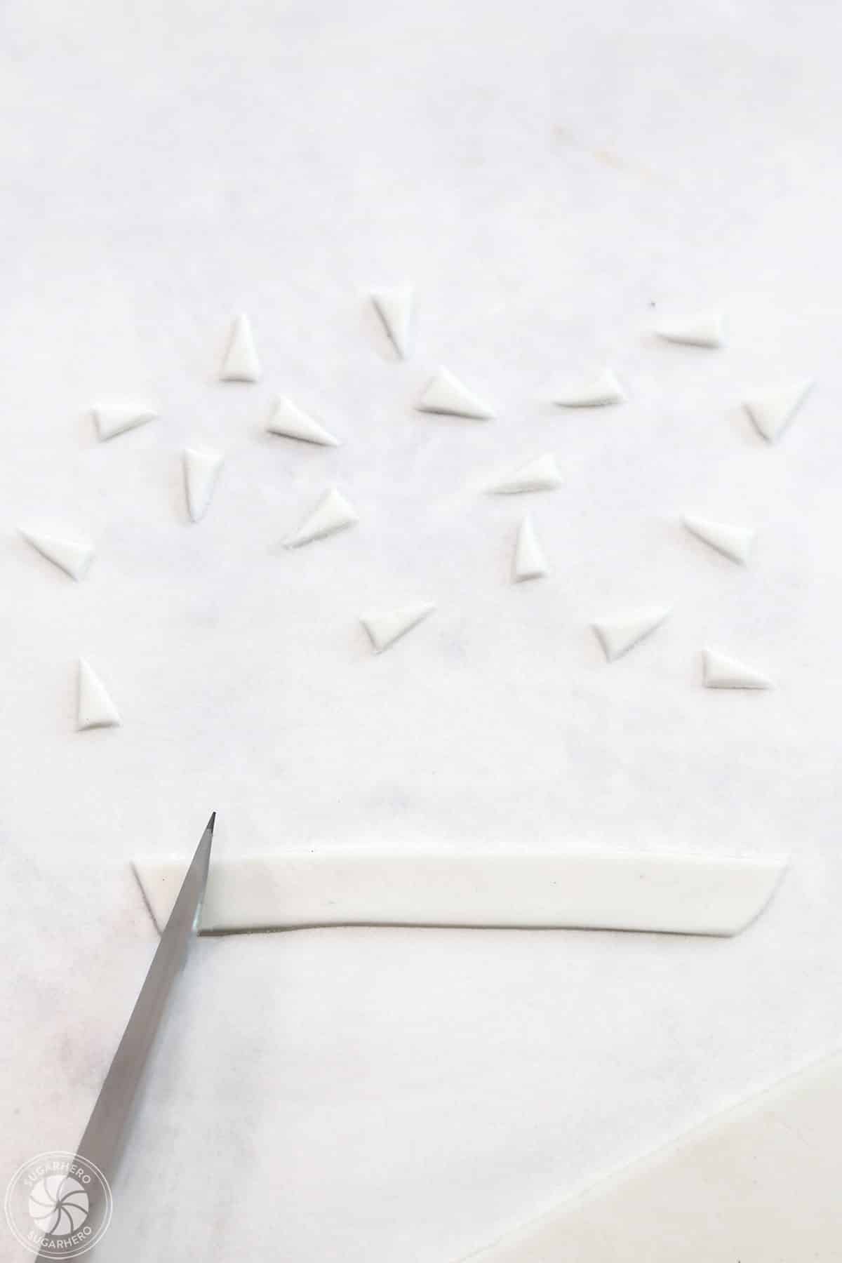 A sharp knife cutting white fondant into triangles to make vampire teeth.