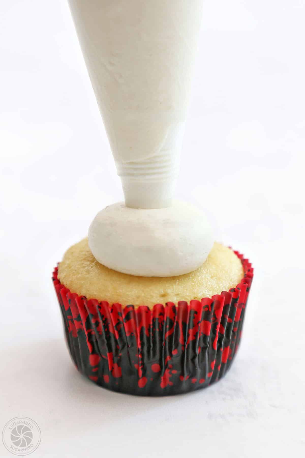 Piping a round ball of buttercream on top of a cupcake.