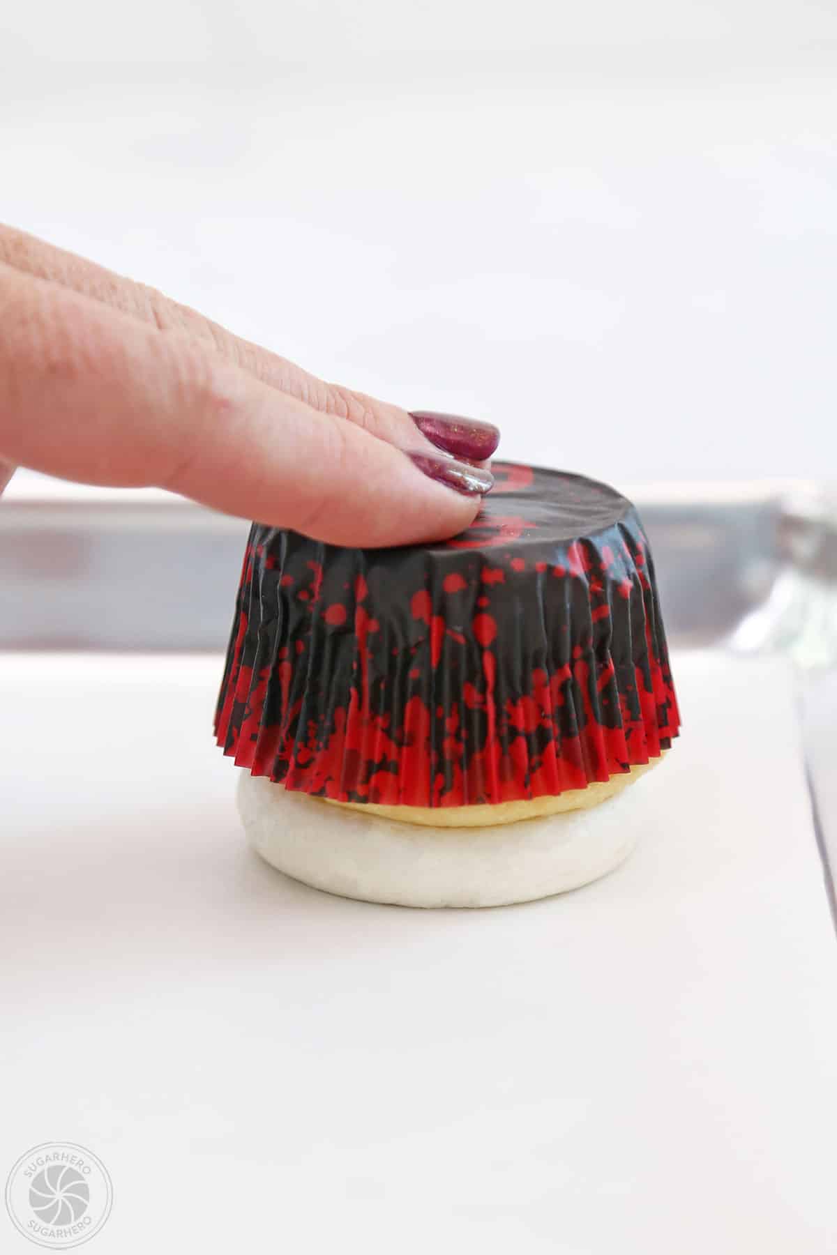 Hand pressing a frosted cupcake onto parchement paper to flatten the top.